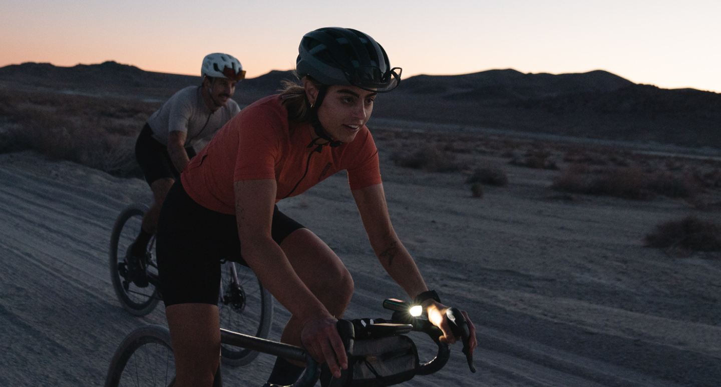 Male and Female riding gravel bikes at dusk with bike headlights on 